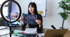 A woman vlogger discusses stock market trends using charts in a home studio.