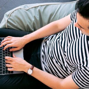 A man in a striped shirt using a laptop on a bean bag, embodying relaxed productivity.