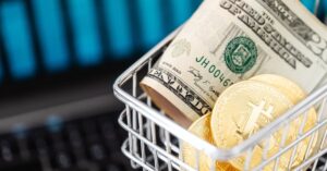 Close-up of bitcoin coins and US dollars in a shopping cart on a laptop, symbolizing digital finance.